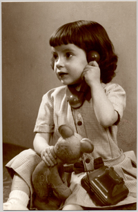 [Niñita de melena con vestido cuadrillé hablando por teléfono y un juguete en sus manos]