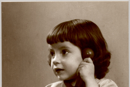 [Niñita de melena con vestido cuadrillé hablando por teléfono y un juguete en sus manos]