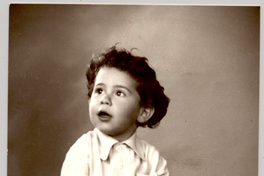 [Niñito de pantalón corto, camisa, sandalias y soquetes blancos, pelo ondulado peinado hacia atrás, sentado sobre un felpudo]