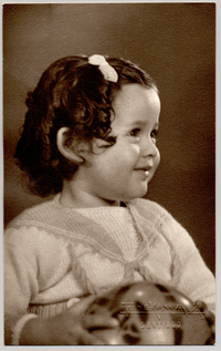 [Niña de cara sonriente, rizos tomados con un pinche, con un traje de lana y una pelota en sus manos]