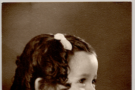 [Niña de cara sonriente, rizos tomados con un pinche, con un traje de lana y una pelota en sus manos]