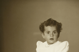 [Niñita de vestido blanco con el Pato Donald de juguete, sentada sobre una piel blanca]