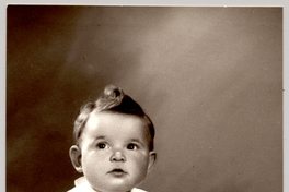 [Guagua rubia con el pelo tomado hacia arriba, vestido mangas cortas, con una pelota y sentada sobre un felpudo]