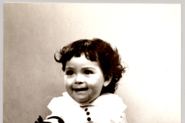 [Niñita sonriente sentada sobre un plumón de brocato con un juguete en sus manos]