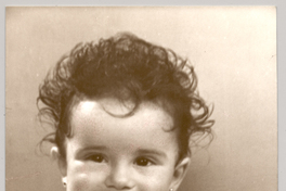 [Bebé [niña] con vestido recogido color blanco con mangas cortas englobadas, pelo ondulado y con un dedo en la boca]