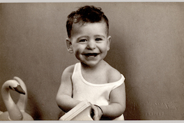 [Niño soriente con camiseta blanca sin mangas y un teléfono de juguete en sus manos y sentado con la misma polera y pantalón oscuro]