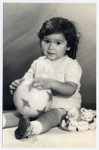 [Bebé de unos dos años sentada con una pelota en sus manos y otros juguetes]