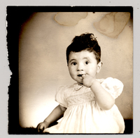 [Niña de vestido blanco con mangas englobadas con la mano metida en la boca]