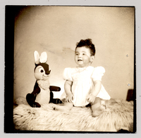 [Niña de vestido blanco con mangas englobadas sentada con un felpudo y con un conejo de peluche]