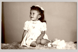 [ Niña de vestido blanco veraniego y cinta en el pelo sentada sobre un felpudo]