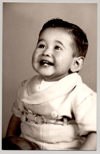 [Niñito de pantalón corto con cinturón sentado sobre un felpudo con una pelota y sonriendo]