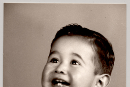 [Niñito de pantalón corto con cinturón sentado sobre un felpudo con una pelota y sonriendo]