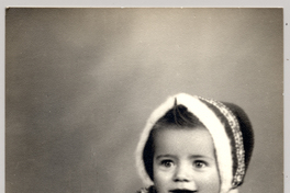 [Niñita con abrigo y un gorro de lana de colores sentada sobre un felpudo]