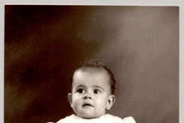 [Niñita de vestido recogido con una cinta blanca, mangas cortas englobadas y descalza sentada sobre un felpudo]