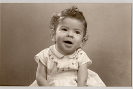 [Niñita de pelo rubio risado, vestido blanco bordado en la pechera y amarrado en la cintura]