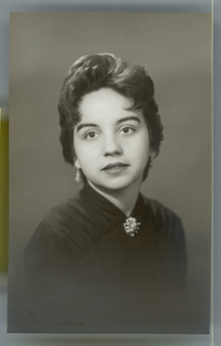 [Mujer joven de vestido negro, prendedor en el cuello y aros]