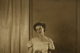 [Mujer joven de vestido largo con una gran rosa en la cintura y un collar de flores en el cuello]