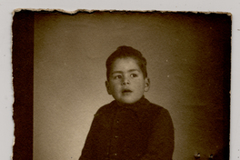 [Niño regordete y tes morena con chaleco oscuro posando sentado]