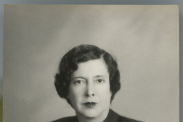 [Mujer de traje dos piezas y blusa abotonada negra, uñas pintadas rojas, sentada con las manos una encima de la otra]