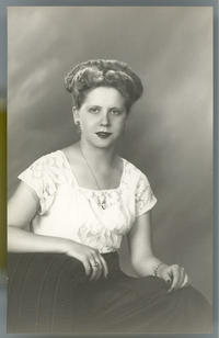 [Mujer joven de pelo claro, blusa de broderí blanca, falda negra amplia, sentada en un sillón de estudio]