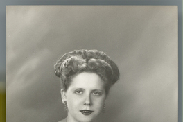 [Mujer joven de pelo claro, blusa de broderí blanca, falda negra amplia, sentada en un sillón de estudio]