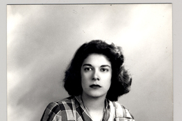 [Mujer joven de tez morena, sentada mirando de frente y de cuerpo entero, pelo ondulado, vestido camisero a cuadros]