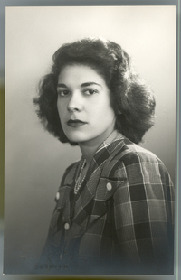 [Mujer joven de tez morena, pelo ondulado, vestido camisero a cuadros, posando de medio cuerpo y de lado]