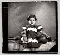 [Niñita de vestido rojo y blanco, con una pelota y un pato de juguete en sus manos mirando de frente]