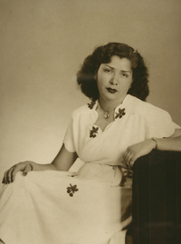 [Mujer de vestido blanco estampado con flores oscuras y un prendedor en el cuello]