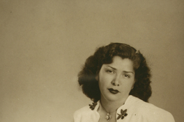 [Mujer de vestido blanco estampado con flores oscuras y un prendedor en el cuello]