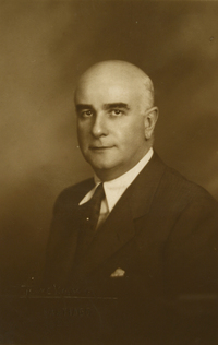 [Hombre semi calvo y canoso vestido con traje oscuro elegante]