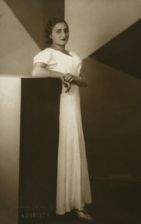 [Mujer joven con rasgos árabes, está de pie, con vestido largo de manga corta color blanco]