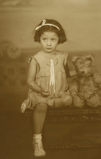 [Niñita sentada en un baúl con un osito de peluche]