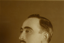 [Hombre posando de perfil, con traje oscuro y un prendedor en la solapa del vestón, de estilo elegante]