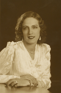 [Mujer joven, vestida elegantemente con una blusa blanca de seda, pelo risado, labios rojos, aros grandes y un collar en su cuello]