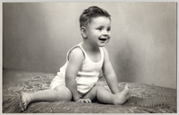 [Niño sentado con las piernas abiertas con una polera blanca sin mangas y sonriendo]