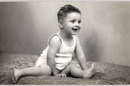 [Niño sentado con las piernas abiertas con una polera blanca sin mangas y sonriendo]