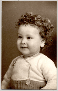 [Niñita de pelo crespo rubio rizado, cara regordeta, sonriente, con un traje de lana abotonado]