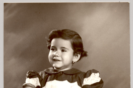 [Niñita de vestido rojo y blanco, con una pelota y un pato de juguete en sus manos mirando hacia el lado]