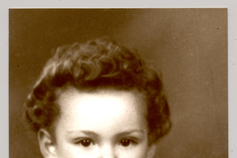 [Niñito pelo onduldo, chaleco abotonado con dibujos,camisa cuello blanco con una figura en sus manos]