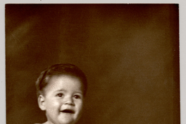 [Bebé desnudo sentado sobre un felpudo con un juguete sobre sus piernas]