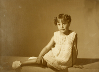 [Niñita rubia de vestido color blanco de hilo grueso y zaptillas blancas, sentada con las piernas hacia el lado]