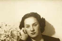 [Mujer joven sentada y apoyada sobre un mueble con un jarro de flores]