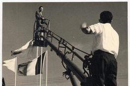 [Domingo Ulloa, con su cámara fotográfica, suspendido en el aire sobre una escalera mecánica para tener visión panorámica de la Exposición Ganadera de la Quinta Normal].