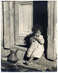 [Niñita de pies descalzos, sentada sobre el umbral de la puerta de su casa en Pomaire]