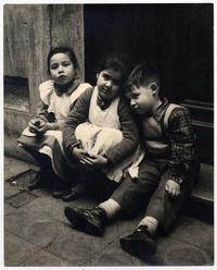 [Tres niños vecinos, sentados en el umbral de la puerta de una casa]