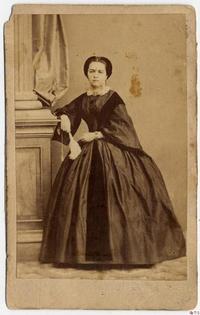 [Dama que sostiene un abanico cerrado, posa de pie y apoya su brazo sobre una columna]