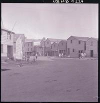 [Personas reunidas en las puertas de sus casas en una calle de pueblo]