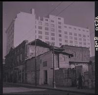 [Transeúntes por una calle con casas antiguas en demolición contiguo a edificio de departamentos]