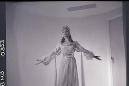 [Bailarina de ballet, caracterizada para una obra, posando de pié con los brazos extendidos]